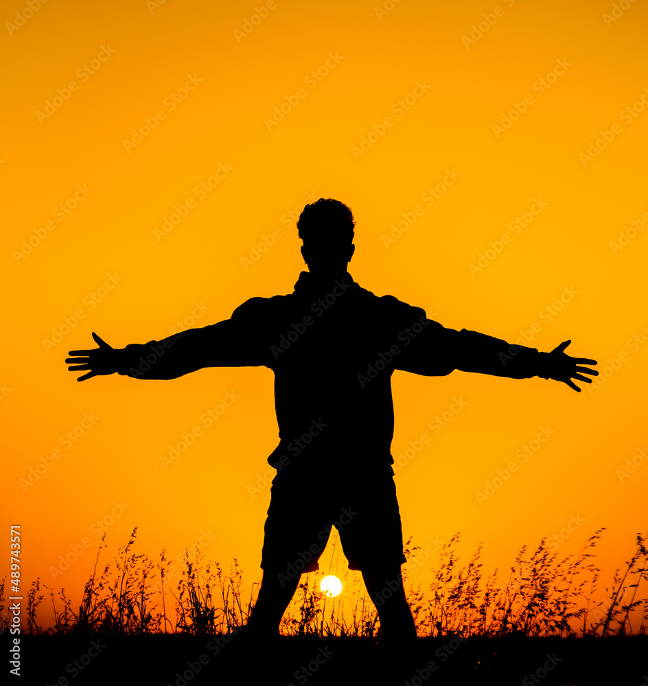 Boy in silhouette with arms raised and open facing the sunset. He is in a natural park feeling free and being able to breathe fresh air Boy in silhouette with arms raised and open facing the sunset. He is in a natural park feeling free and being able to breathe fresh air