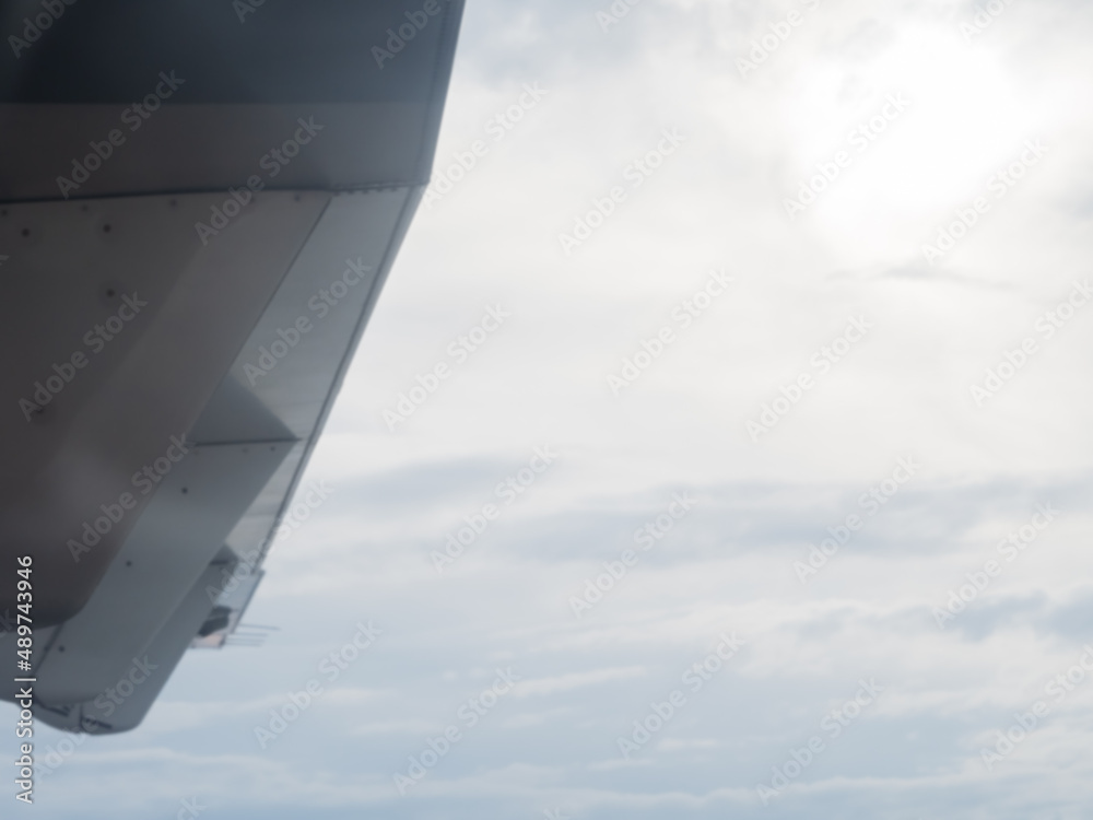 Obraz premium A fragment of the wing of a flying aircraft against the background of a cloudy sky and the sun peeking through the haze. View from the porthole. Soft focus