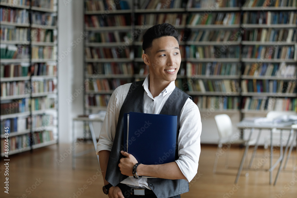 Thoughtful young handsome Z generation male Asian student holding folder with study papers in hands, posing in library, looking in distance visualizing successful future career, feeling motivated. Thoughtful young handsome Z generation male Asian student holding folder with study papers in hands, posing in library, looking in distance visualizing successful future career, feeling motivated.