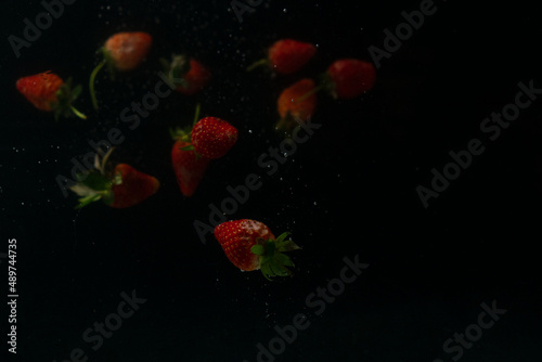 Strawberries falling into water with splash on black background