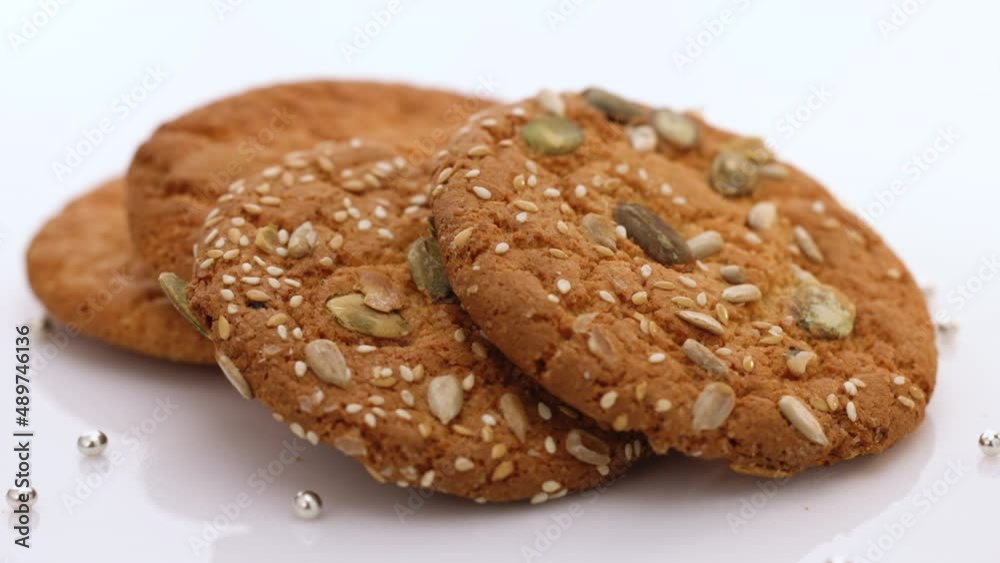 Wheat fall on dietary cookies. Eat oatmeal cookies. Oatmeal cookie rotation on the table with sesame seeds on white background. The concept of making chip cookies Wheat fall on dietary cookies. Eat oatmeal cookies. Oatmeal cookie rotation on the table with sesame seeds on white background. The concept of making chip cookies