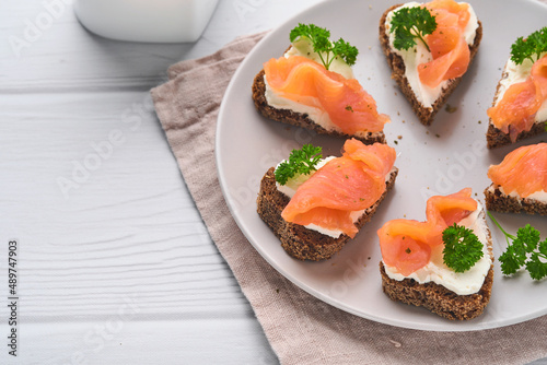 Mini sandwiches with salmon, curd cheese, parsley and rye bread in form of hearts. Valentine's day homemade creative food. Love breakfast design. Selective focus and copy space