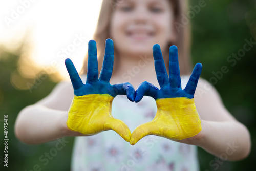 Heart shape with child hands of kid body language for children love, kindness, patriot love concept. Heart hand over sunset sky bokeh background painted in Ukrainian flag colors photo