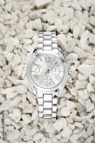 Silver watch with light dial buried in white pebbles