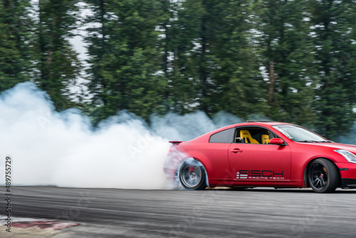 Red Drift Car / Race car drifting around corner very fast with lots of smoke from burning tires on speedway / racetrack / drift track. Infiniti g35 v8. JDM car. Luxury red sport car.  © Tamara