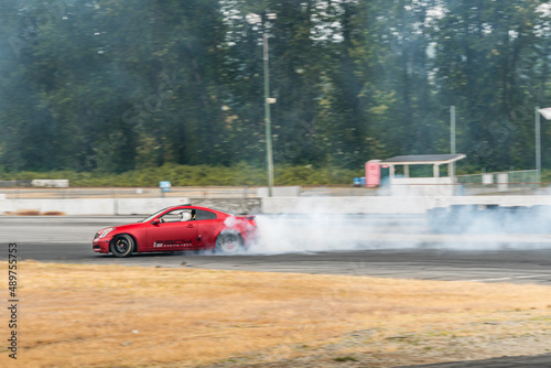 Red Drift Car / Race car drifting around corner very fast with lots of smoke from burning tires on speedway / racetrack / drift track. Infiniti g35 v8. JDM car. Luxury red sport car. 