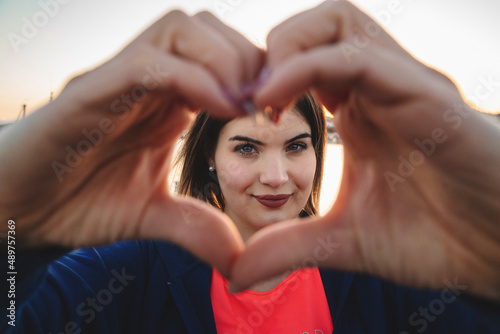 Happy curvy woman framing her face with an heart shape with fingers - self acceptance and self esteem concept photo