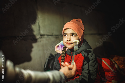 Mom feeds her little daughter while they sit out the attack of the Russian aggressor in a bomb shelter. Terrorism and war, current Ukrainian and world history photo