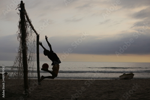 Futebol na praia num fim de tarde. Vê-se a silhueta de uma criança pulando ao defender um gol, com a bola no pé, na beira da praia do sono, em paraty.