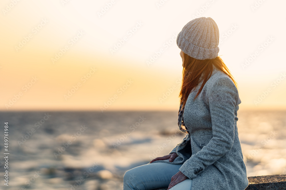 backlighting of a red-haired woman sitting on the breakwater looking at the ocean horizon backlighting of a red-haired woman sitting on the breakwater looking at the ocean horizon