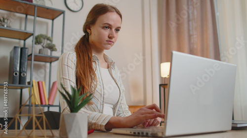 Young woman freelancer using laptop computer typing on keyboard sitting at table working from home office. Adult girl businesswoman e-learning, browsing internet, online shopping, remote job in room