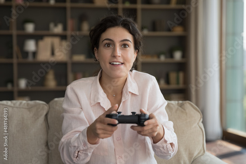 Addicted to modern technology joyful young Hispanic woman using remote controller playing video games alone at home, enjoying domestic leisure weekend hobby activity, virtual reality concept.