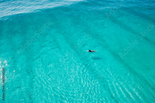 Surfer on surfboard in transparent ocean waiting wave. Aerial view