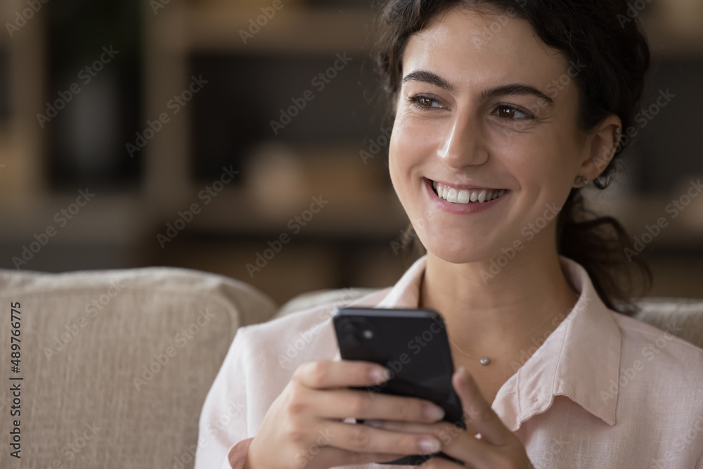 Head shot close up happy beautiful millennial Hispanic woman with smartphone in hands looking in distance, feeling excited using interesting mobile applications, communicating online, web surfing. Head shot close up happy beautiful millennial Hispanic woman with smartphone in hands looking in distance, feeling excited using interesting mobile applications, communicating online, web surfing.