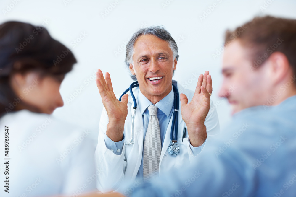 Doctor explaining to his patients. Portrait of happy mature doctor explaining to his young patients. Doctor explaining to his patients. Portrait of happy mature doctor explaining to his young patients.
