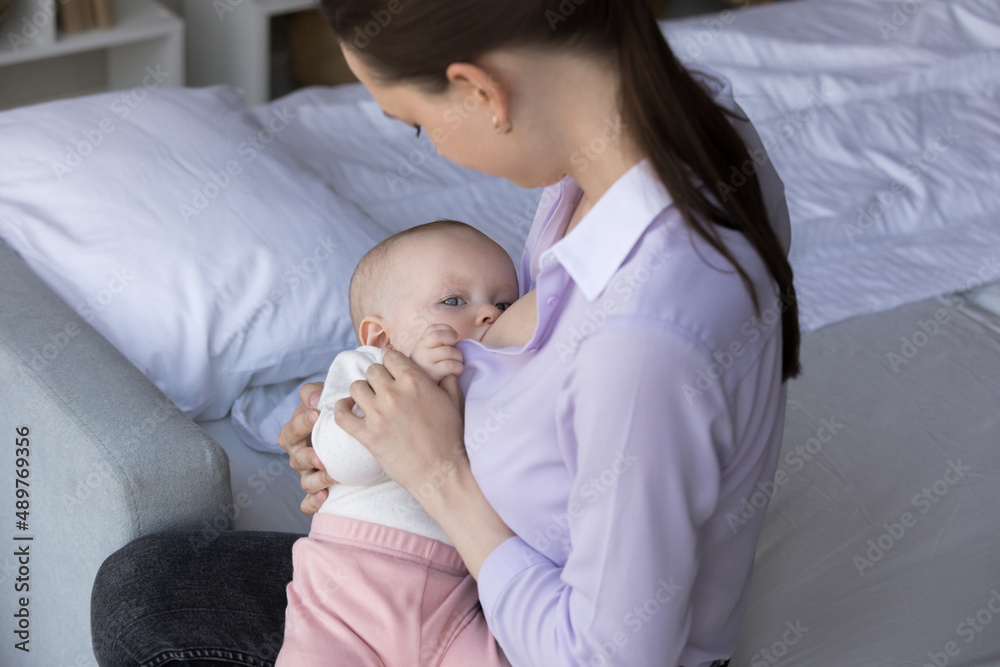 Adorable little hungry infant sucking breastmilk from mom breast