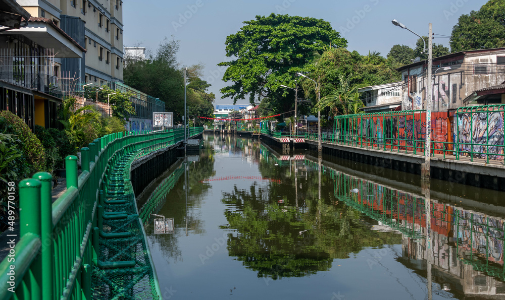 Canal, or khlong, in downtown Bangkok with sidewalks and reflections in the water