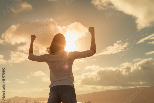 Strong and determined young woman flexing her arms up to the sunset sky. People power, and strength concept