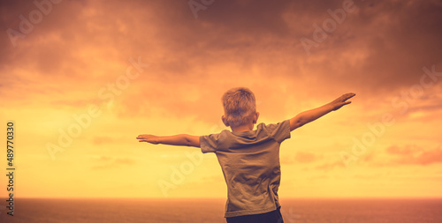 Happy little boy with arms outstretched facing a sunset background. Freedom and happiness concept 