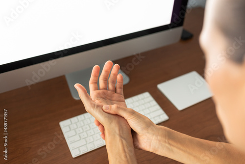 woman suppering from carpal tunnel, syndrome holding  touching her hand while working with laptop in the office.  photo