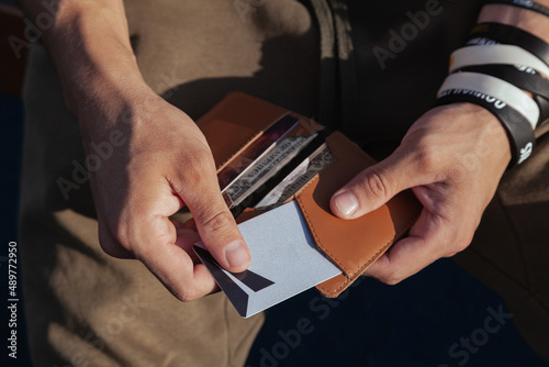 A young man in sportswear is holding a small comfortable red leather wallet in his hands and takes out a plastic card, top view. Horizontal orientation, copy space, close-up, no face