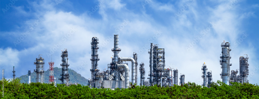 © Kalyakan - Oil refinery plant from industry zone, Oil and gas petrochemical industrial with tree and blue sky background, Refinery factory oil storage tank and pipeline steel, Ecosystem and healthy environment.