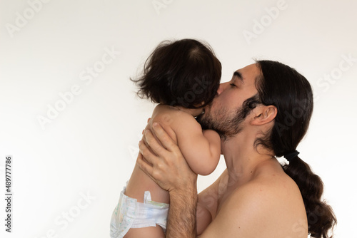 portrait of a hispanic father and son kissing on the cheek on a white background