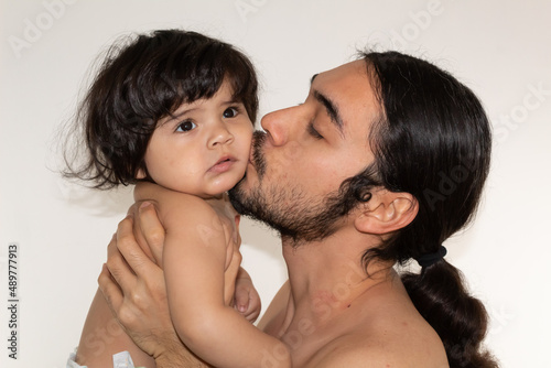 portrait of a hispanic father and son kissing on the cheek on a white background