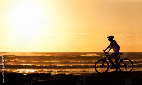Cycling off into the sunset. A silhouette of a female cyclist on the beach at sunset.