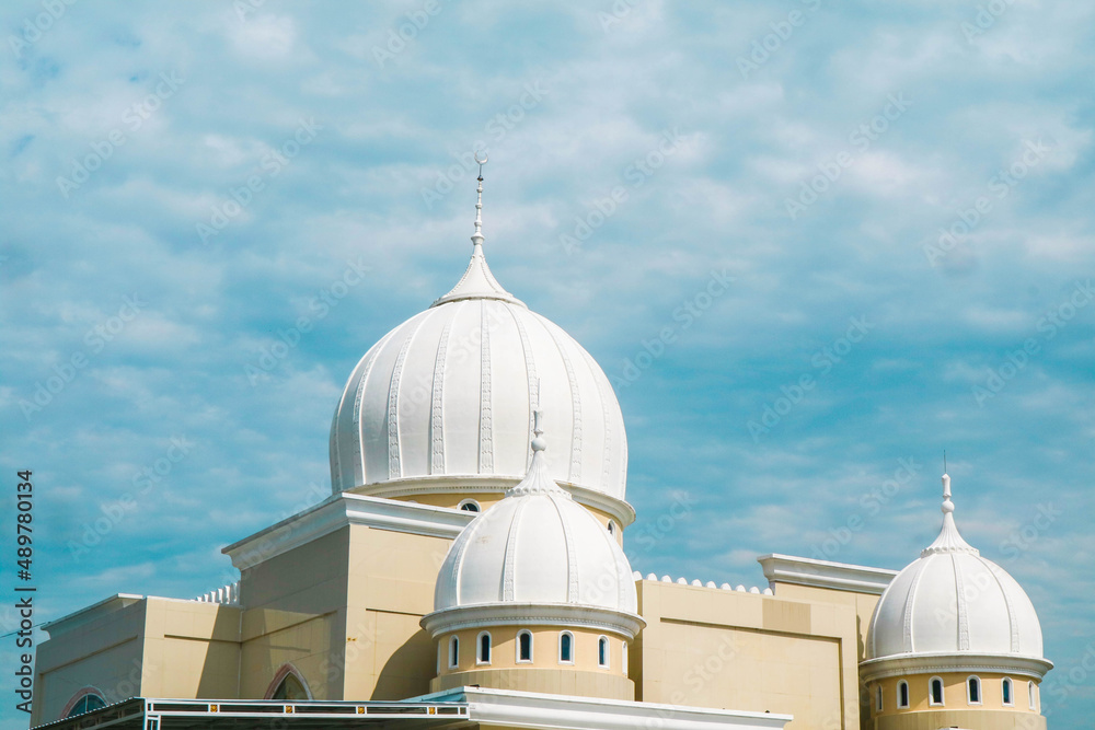 Cloudy clear blue sky over a mosque. Islamic praying building. Crescent on white covered dome and minaret.;