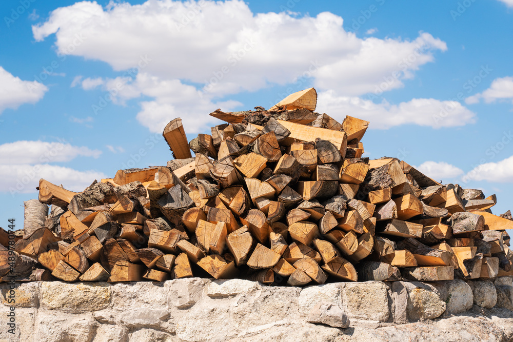 A pile of logs for the stove stacked on top of each other against the blue sky