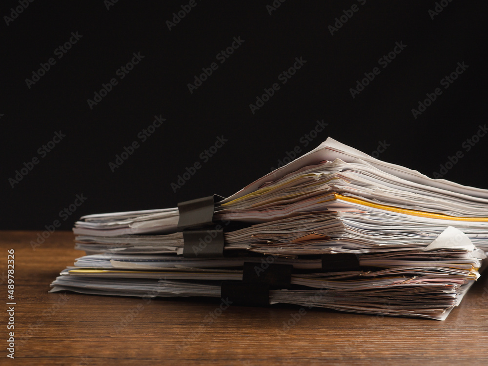 Stack of documents with binder clips on a wooden table with a black background Stack of documents with binder clips on a wooden table with a black background