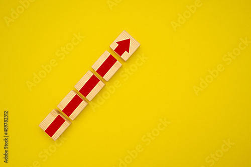 Wooden blocks with red arrow up over a yellow background. Business growth concept