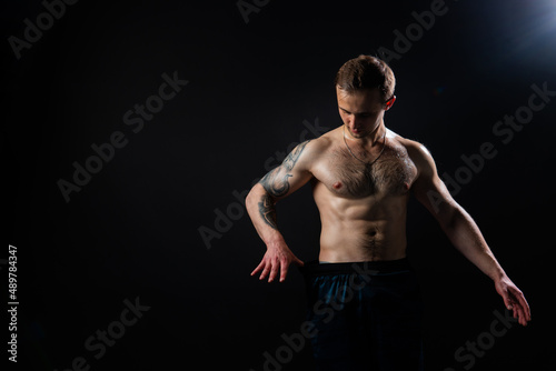 Man on black background keeps dumbbells pumped up in fitness bodybuilding black, muscular man bodybuilder powerful, weightlifting. skin gym fit Look at the press and measures the size of pants for