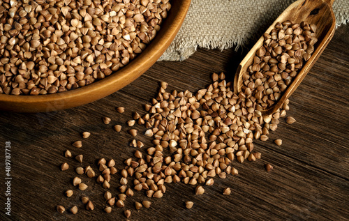 Organic buckwheat groats in a wooden bowl with a spoon on a linen napkin on a wooden table. Banner. Rustic style. Healthy nutrition concept. Buckwheat contains a large amount of vitamins and minerals. © KONSTANTIN