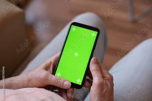 selective focus, Hands of old woman hold vertically phone with green screen. talking online. Person study new technology, work online, communication from home. choice and order online