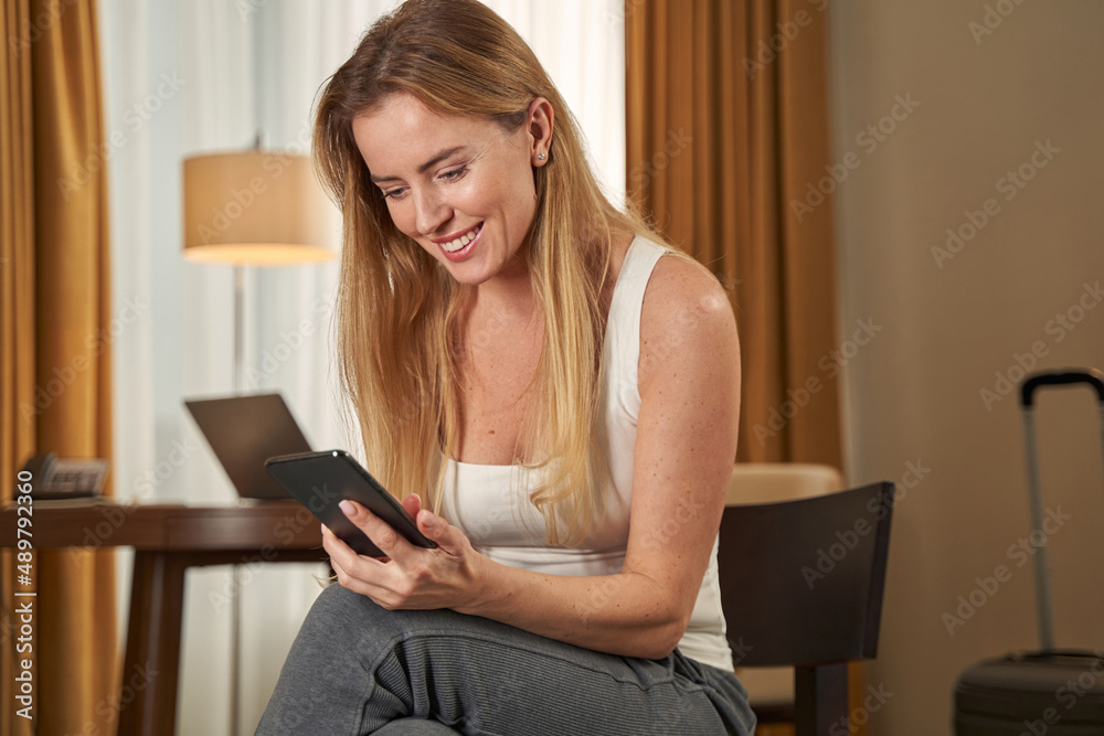 Woman smiling while texting on mobile phone in hotel Woman smiling while texting on mobile phone in hotel