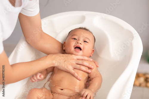 Calm of asian newborn baby bathing in bathtub.mother bathing her son in warm water.Happy adorable newborn infant smile in tub relax and comfortable.Newborn baby care concept
