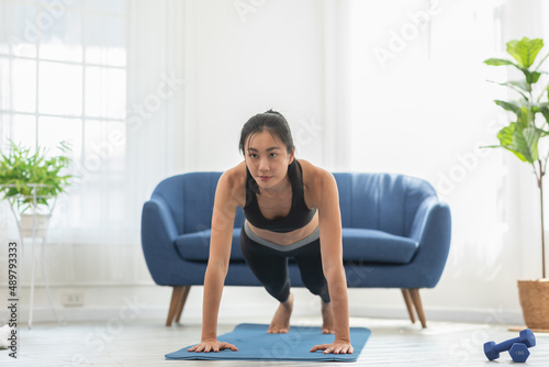 Asian girl doing push ups workout exercise on exercise mats concentration on shoulder muscle at home.Athletic female pushing up training with cardio exercise in living room.Self workout concept