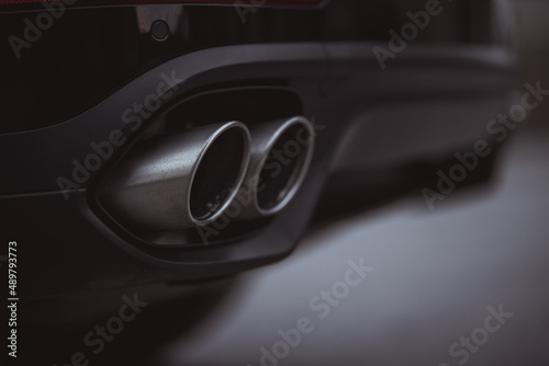Double oval exhaust tips on a modern sport car or SUV. Visible two tailpipes coming out from an opening in the rear bumper. Black color.