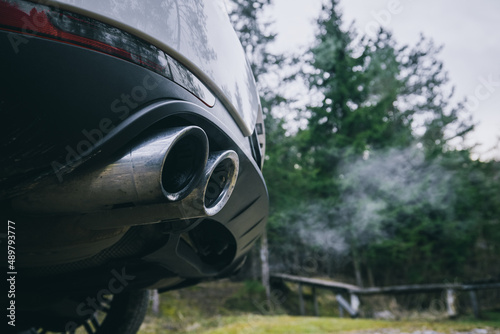 Fototapeta Naklejka Na Ścianę i Meble -  Double oval exhaust tips on a modern SUV car or crossover vehicle. Visible vapour of smoke in green environment. SUV and cars polluting environment.