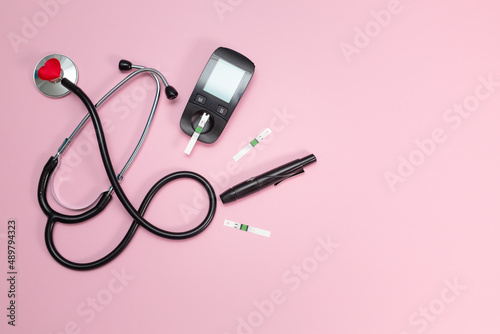 Diabetes equipment, glucose level blood test on pink background with copy space. Diabetic items to control diabetes blood sugar meter, lancet, test strip and lancing device with stethoscope