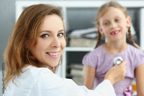 Smiling pediatrician doctor listen to girl breath and heartbeat with stethoscope