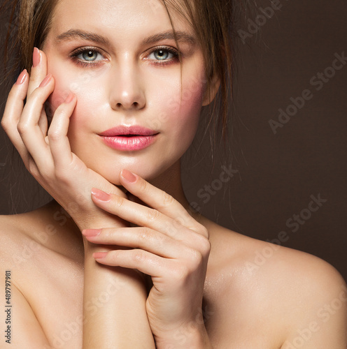 Face Beauty Woman. Model with Full Plump Glossy Lips and Smooth Skin holding Hands with Nude Nail Polish on Cheek over Dark Background