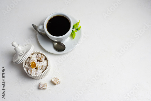 Turkish delight with peanuts in a white vase on a light table. Black hot coffee in a white cup in the background. Top view, space for text