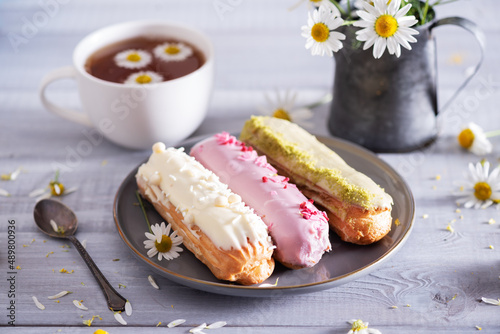Beautiful delicious french eclairs set with original cream decor on white plate on  wooden background. Selective focus. Tasty colorful dessert profiteroles. photo