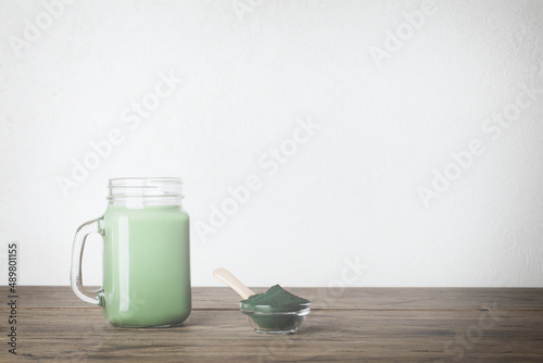 fresh green smoothie in glass bottle and spirulina powder with spoon on wooden background. useful habits  self care and healthy lifestyle. copy space