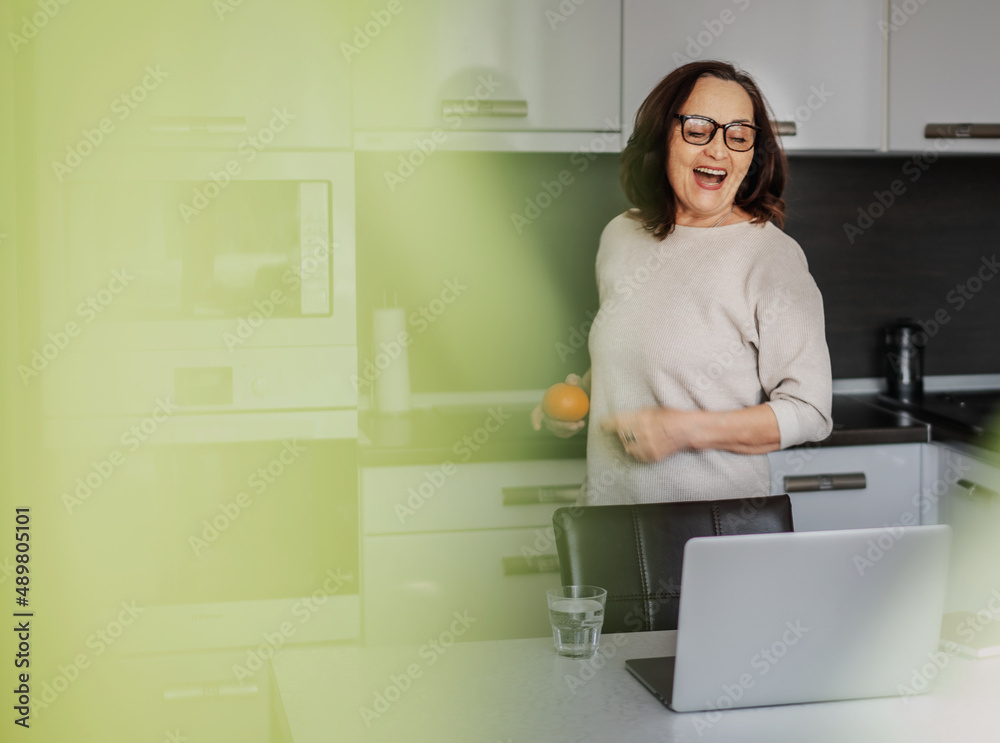 Beautiful happy cheerful elderly woman with a smile and at home in the kitchen in front of a laptop Beautiful happy cheerful elderly woman with a smile and at home in the kitchen in front of a laptop