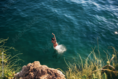 Woman jumping off cliff into the sea. Summer fun lifestyle.