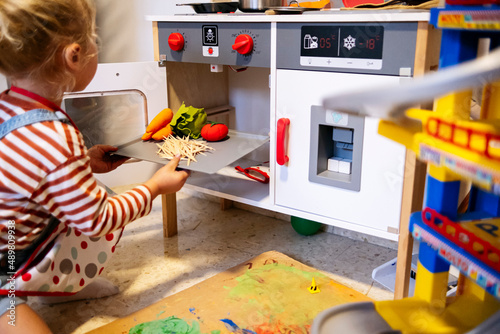 Son putting vegetables tray by oven in toy kitchen at home photo